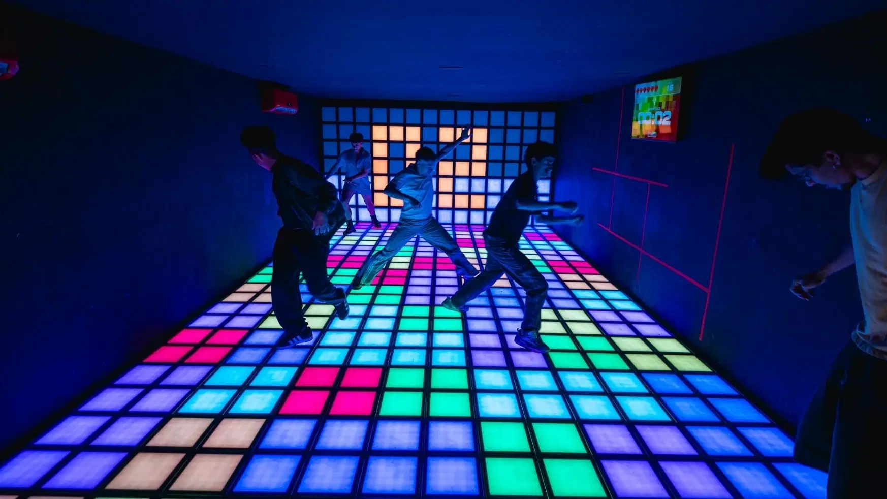 Jogadores jogam o jogo Caça às Cores na sala Max do Arcade Haus Tatuapé e se movimentam no piso interativo